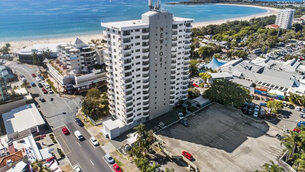 A high-rise hotel with multiple floors, a parking lot, and a view of the beach and ocean.