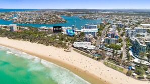 A coastal cityscape with a sandy beach, marina, and various buildings including hotels and a surf club.