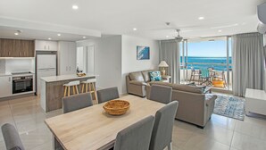 A modern living room with a dining area, kitchen, and a balcony with a view of the sea.