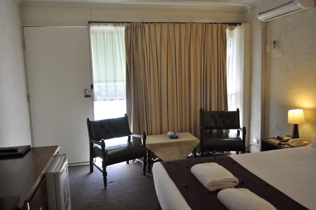 Ein Hotelzimmer mit einem Bett, zwei Stühlen, einem kleinen Tisch, einem Schreibtisch und einer Lampe.