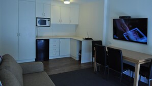 A compact living space with a kitchenette, a flat-screen TV mounted on the wall, a dining table with chairs, and a sofa. - Albury Burvale Motor Inn (Albury)
