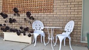 A white metal table and two chairs set against a brick wall with a wooden lattice. - Albury Burvale Motor Inn (Albury)