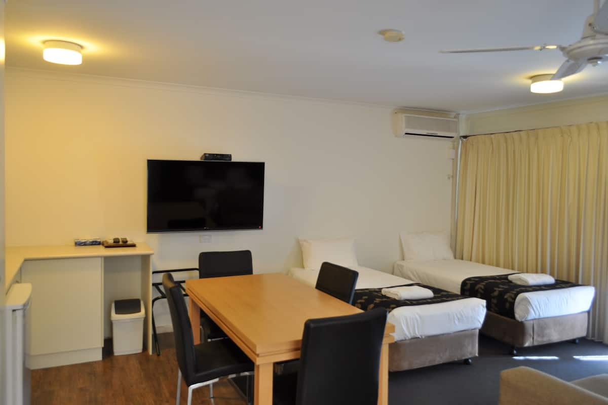 Ein Hotelzimmer mit Holztisch, zwei Betten, Fernseher und Deckenventilator.