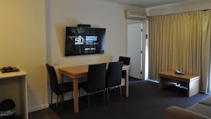 A hotel room with a dining area, a television displaying a program, a small table with a remote control, and a window with curtains. - Albury Burvale Motor Inn (Albury)