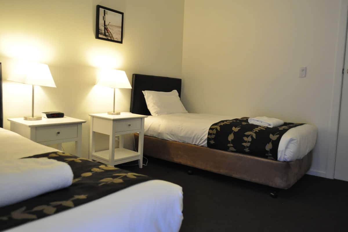 Ein Hotelzimmer mit zwei Betten, jedes mit einer weißen Tagesdecke und einer schwarz-floralen Decke. Zwei Nachttische mit Lampen und ein gerahmtes Bild an der Wand.