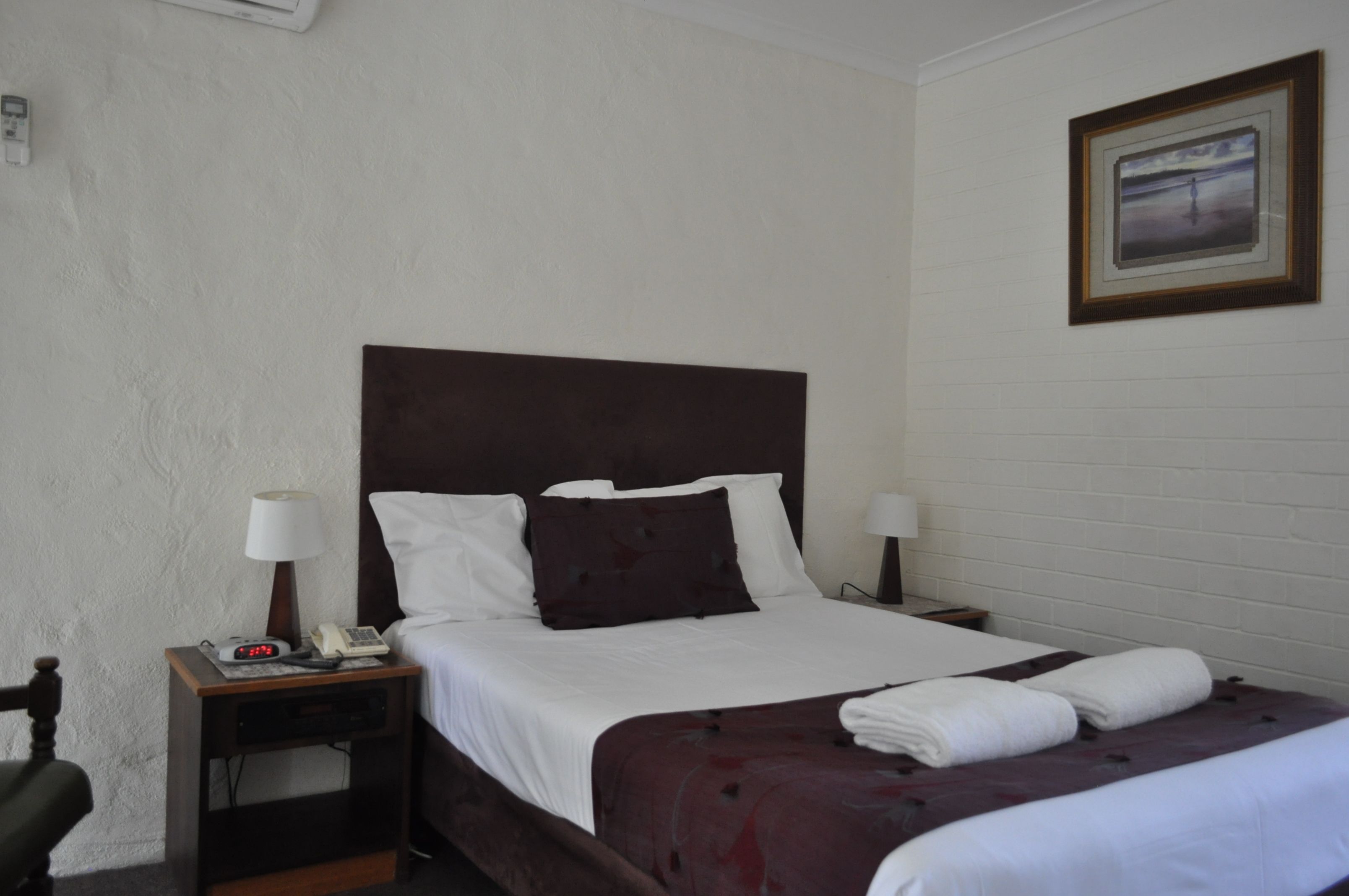 Habitación de hotel con una cama individual, una mesita de noche con teléfono y lámpara, y un cuadro en la pared.