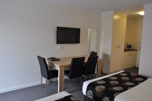 A hotel room with a bed, a desk with chairs, a flat-screen TV, a microwave, and a wardrobe.