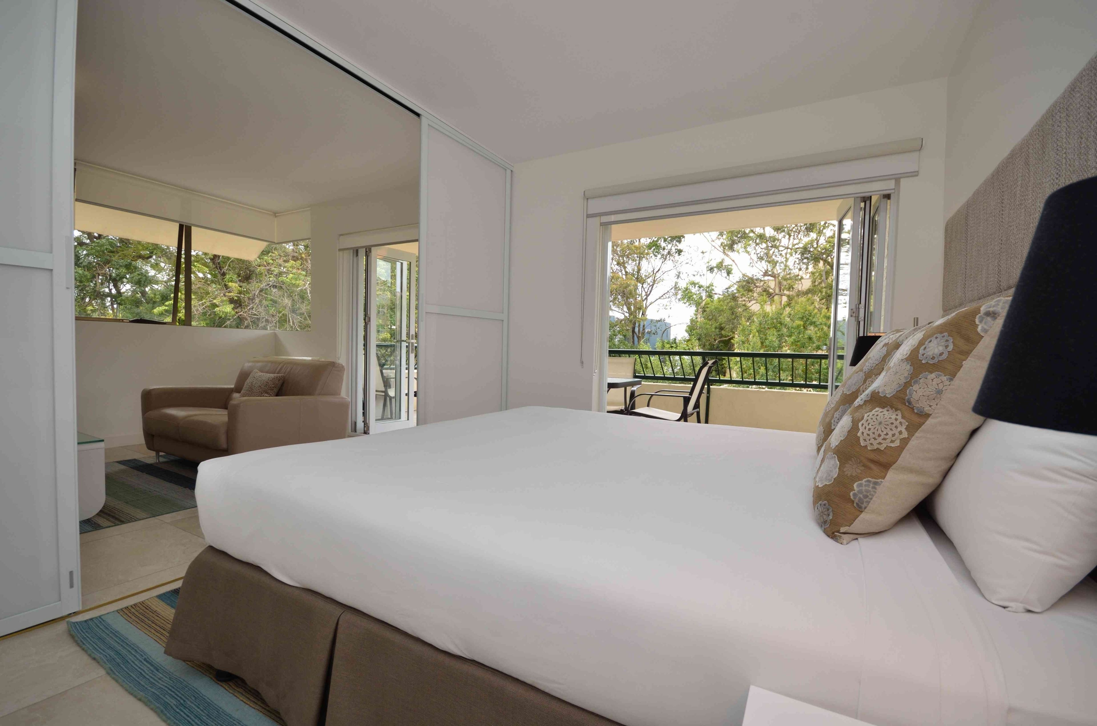 A bedroom with a large bed, a sofa, and a balcony with a view of trees.