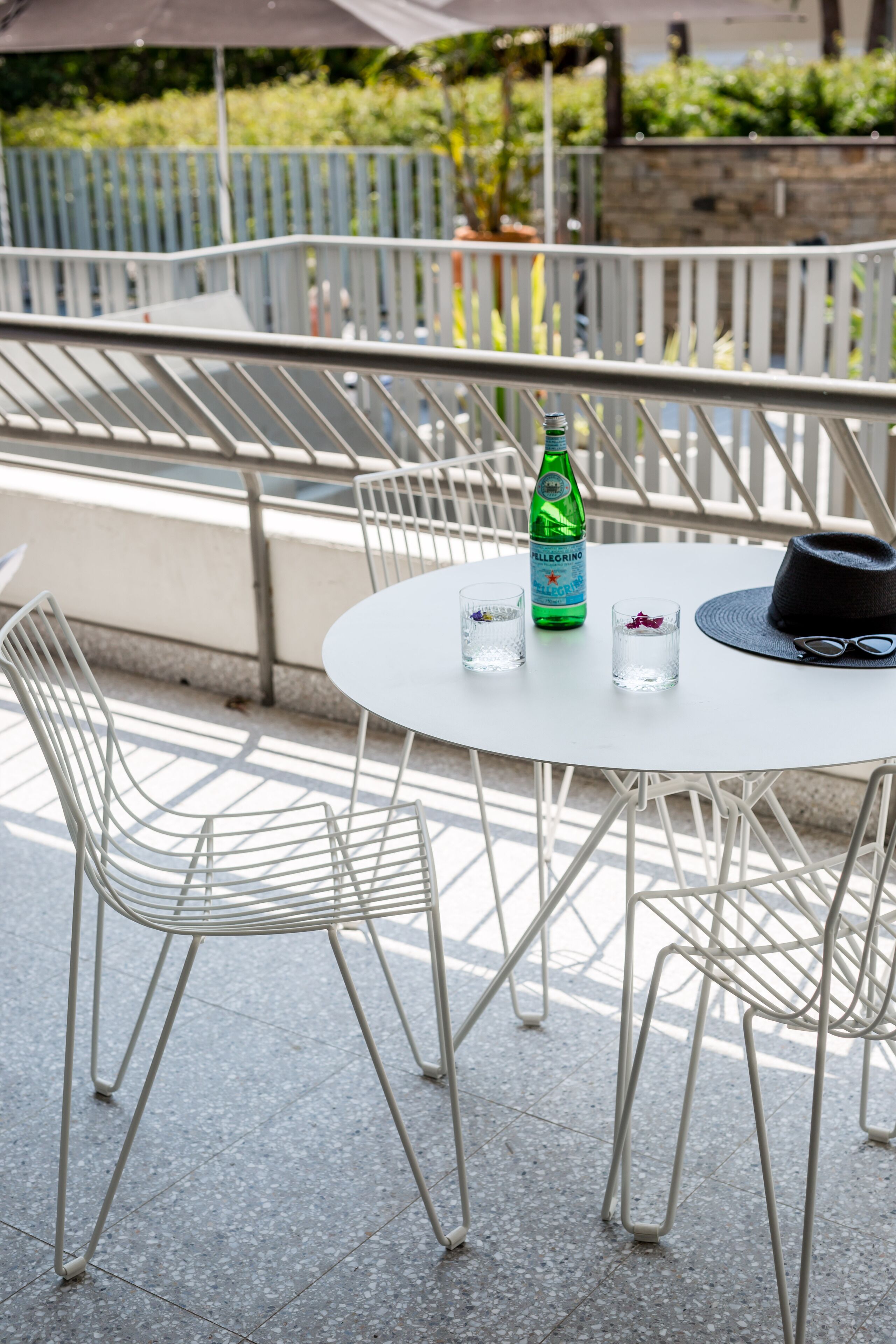 A round table with a bottle and glasses, surrounded by metal chairs.