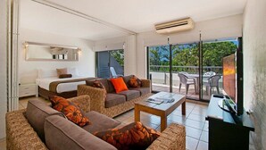 A modern hotel room with a balcony, a bed, a sofa, a coffee table, and a TV. - Saks on Hastings (Noosa Heads)