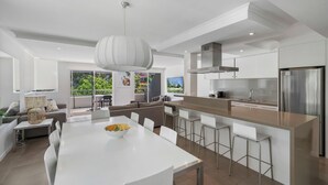 A modern kitchen with a central island, bar stools, and a large window overlooking a garden. - Saks on Hastings (Noosa Heads)