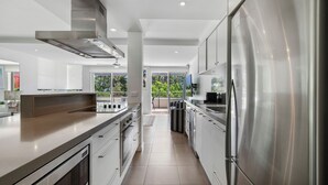 A modern kitchen with stainless steel appliances, a large island, and a view to the outdoors. - Saks on Hastings (Noosa Heads)
