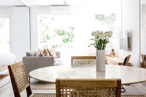 A round dining table with a white vase of white flowers in the center, surrounded by wooden chairs with a woven backrest.