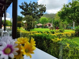 Vista de un jardín cuidado con una mesa de picnic y flamencos, cielo despejado y un edificio al fondo.