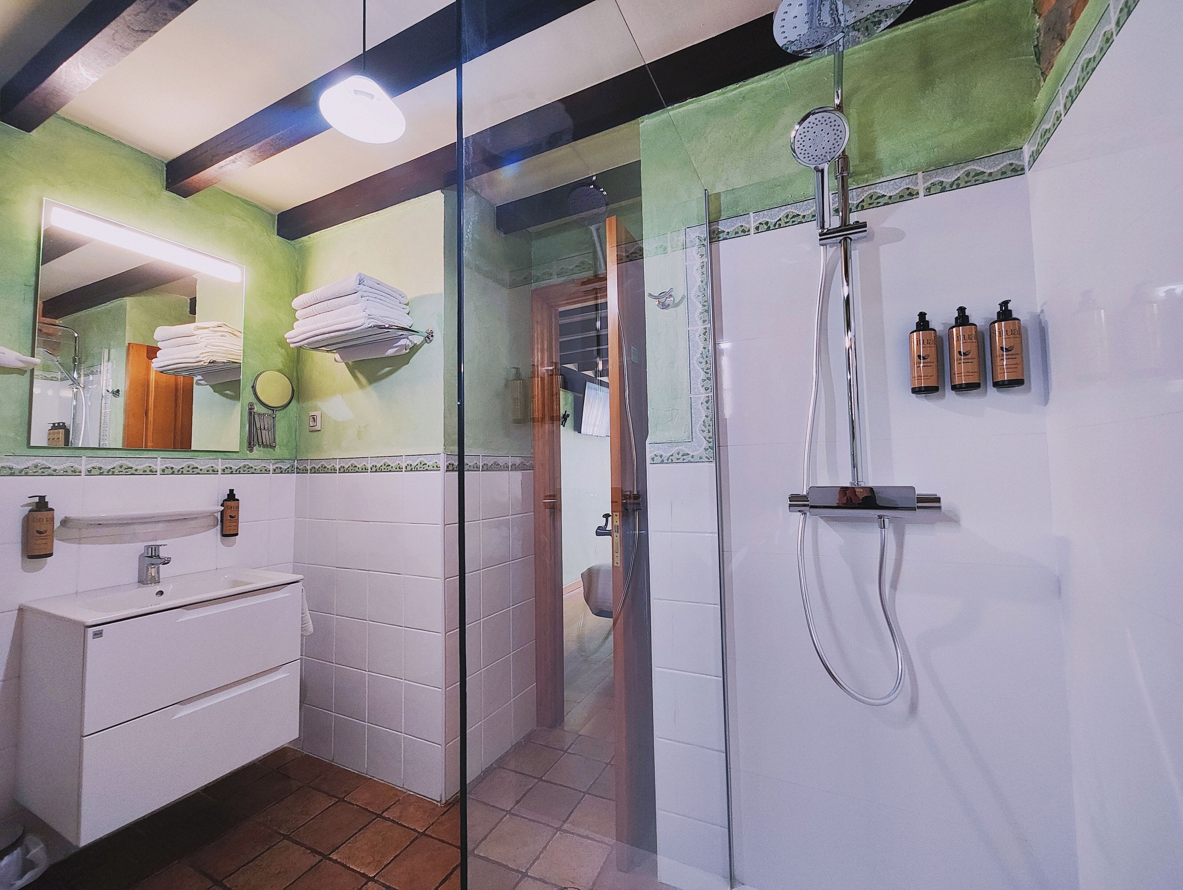 Un baño con ducha de vidrio, lavabo con espejo y artículos de aseo en la pared.