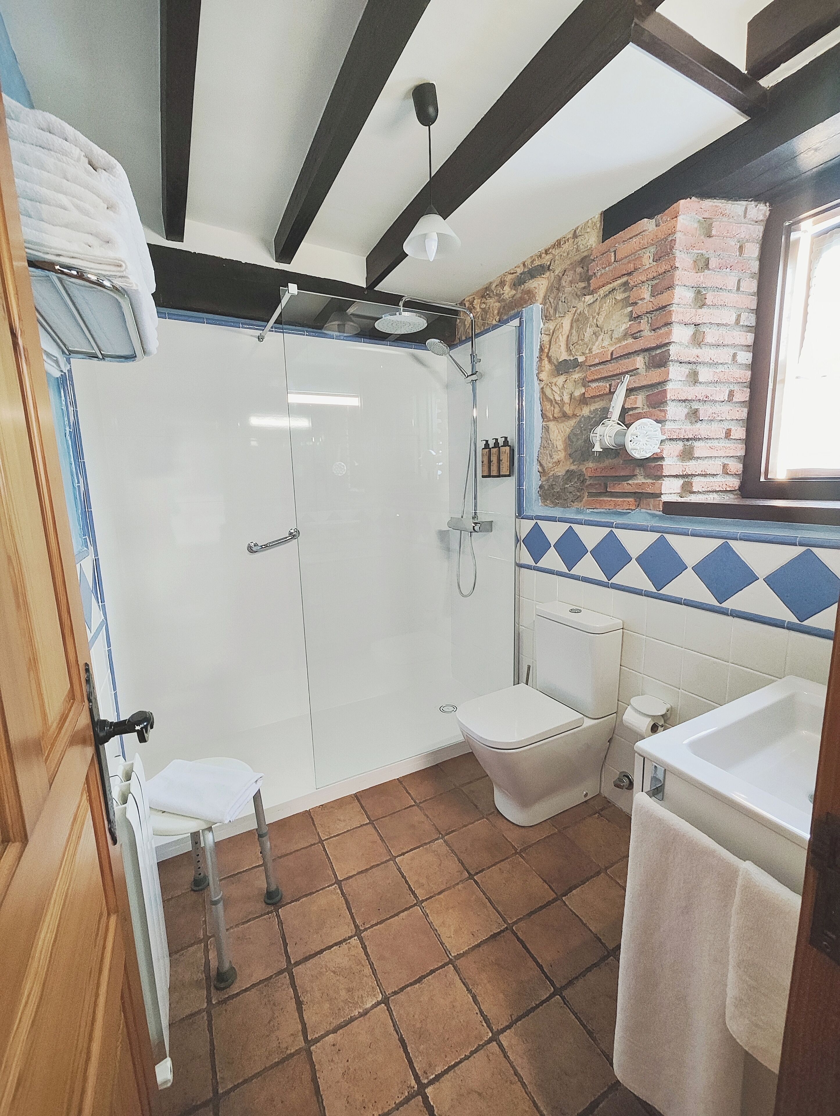 A bathroom with a shower, toilet, and sink, featuring exposed brick walls and a tiled floor.