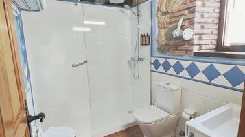 A bathroom with a shower, toilet, and sink, featuring exposed brick walls and a tiled floor.