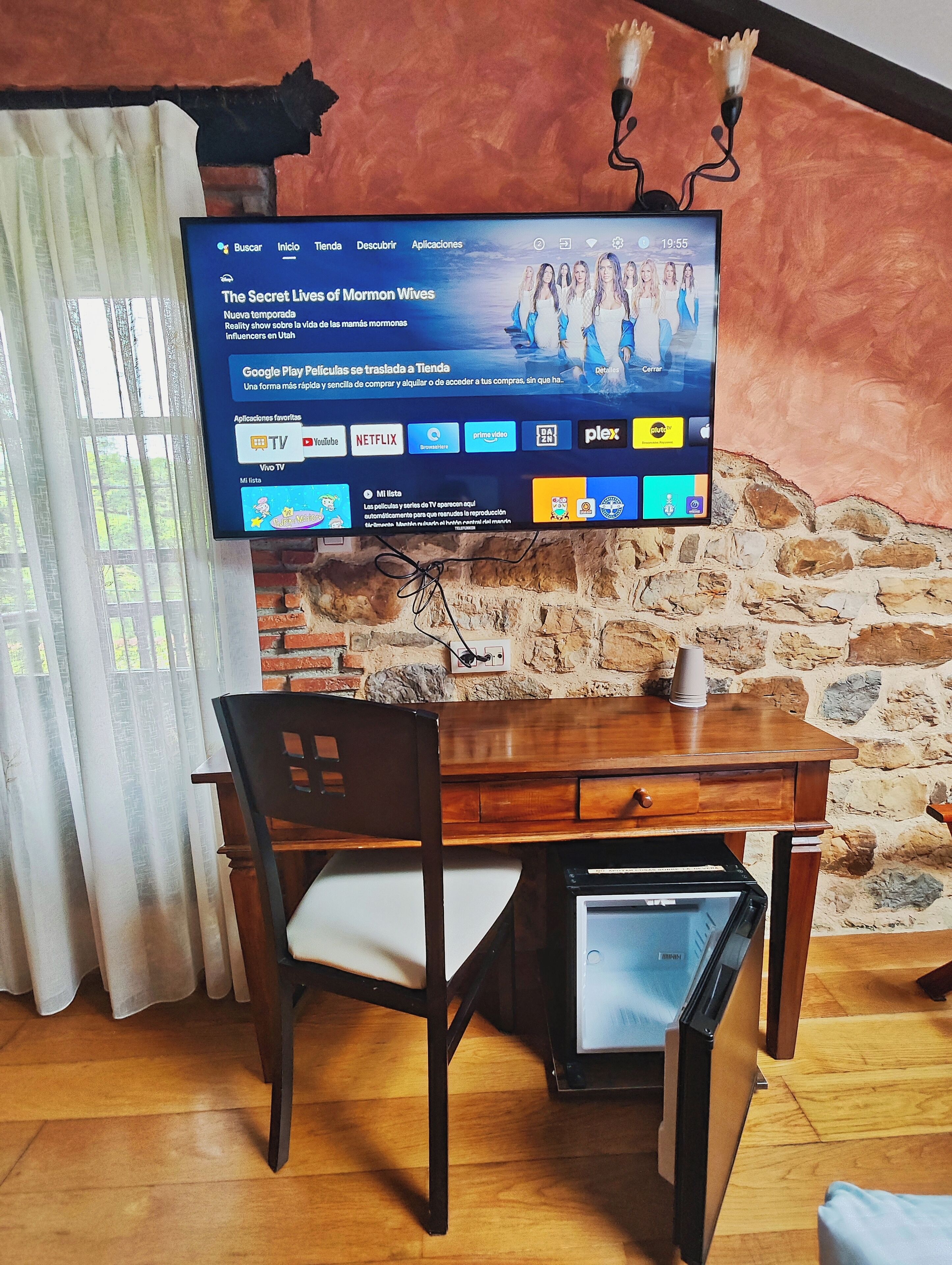 Una sala de estar con televisión montada en una pared de ladrillo, una mesa de madera y una silla.