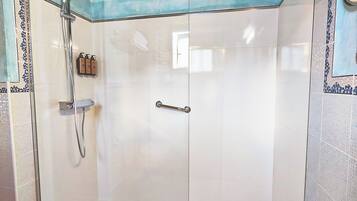 Une douche fermée par des parois en verre, dotée d’un pommeau de douche à main et d’un flexible de douche à main.
