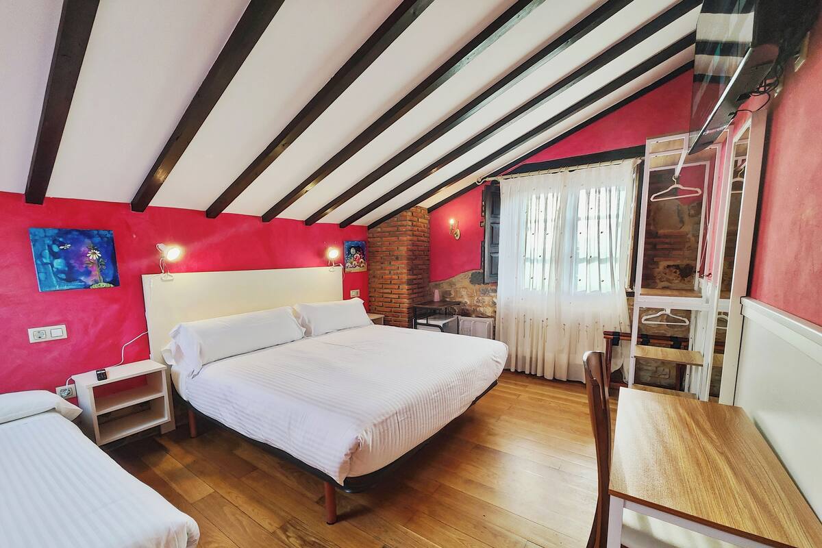Une chambre à coucher avec un lit, des tables de chevet, une chaise, une lampe suspendue, un mur en briques et une fenêtre avec des rideaux.