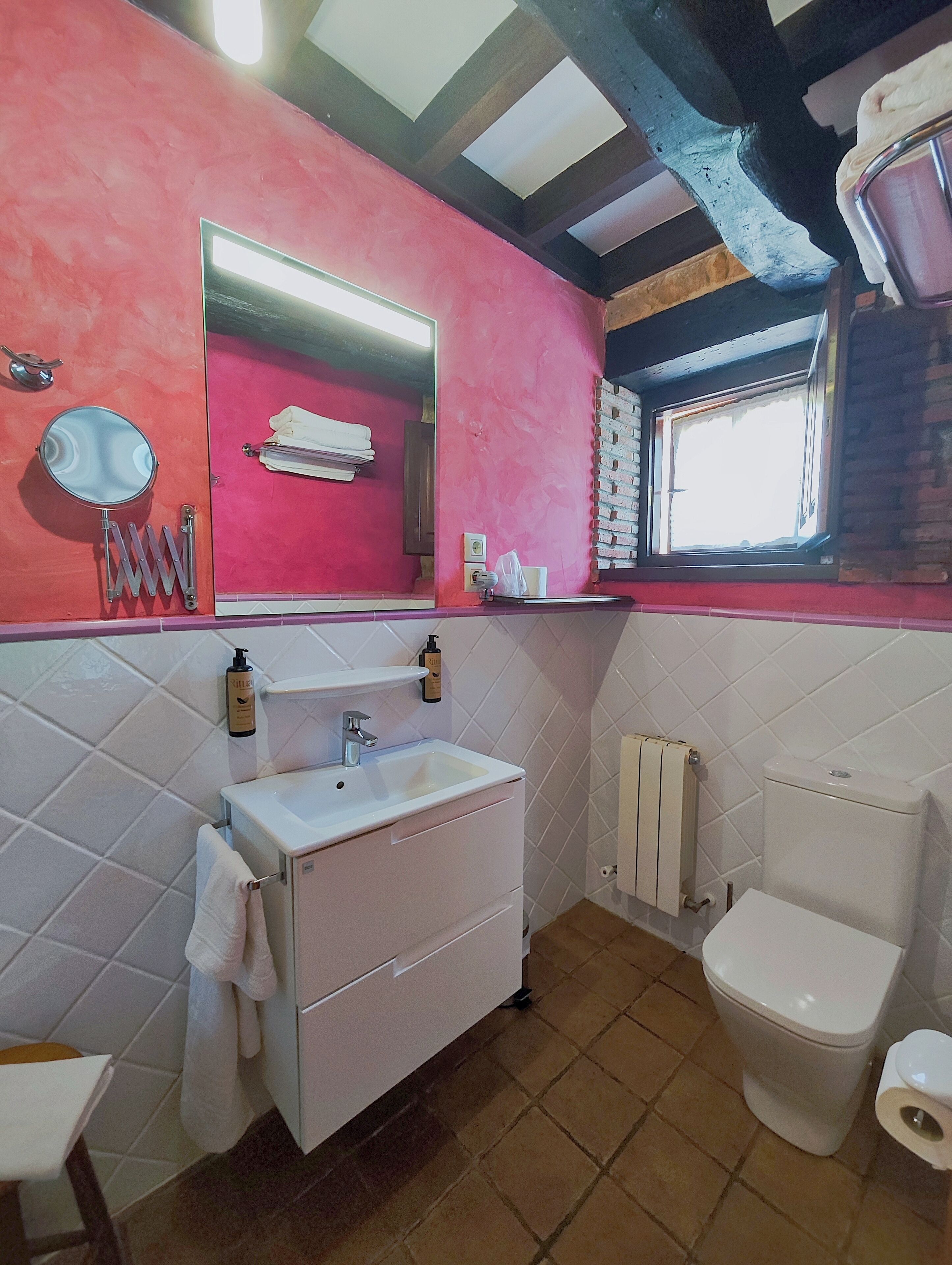 Un baño con lavamanos blanco, un espejo, un inodoro y una ventana.