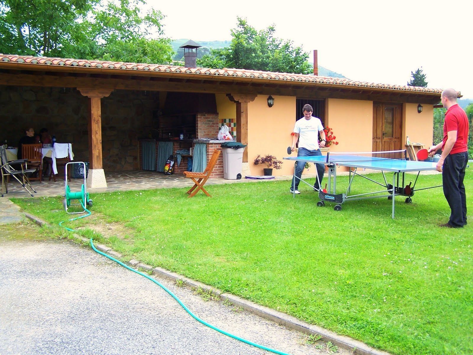 Un espacio exterior con mesa de ping pong, una silla de madera y una manguera.