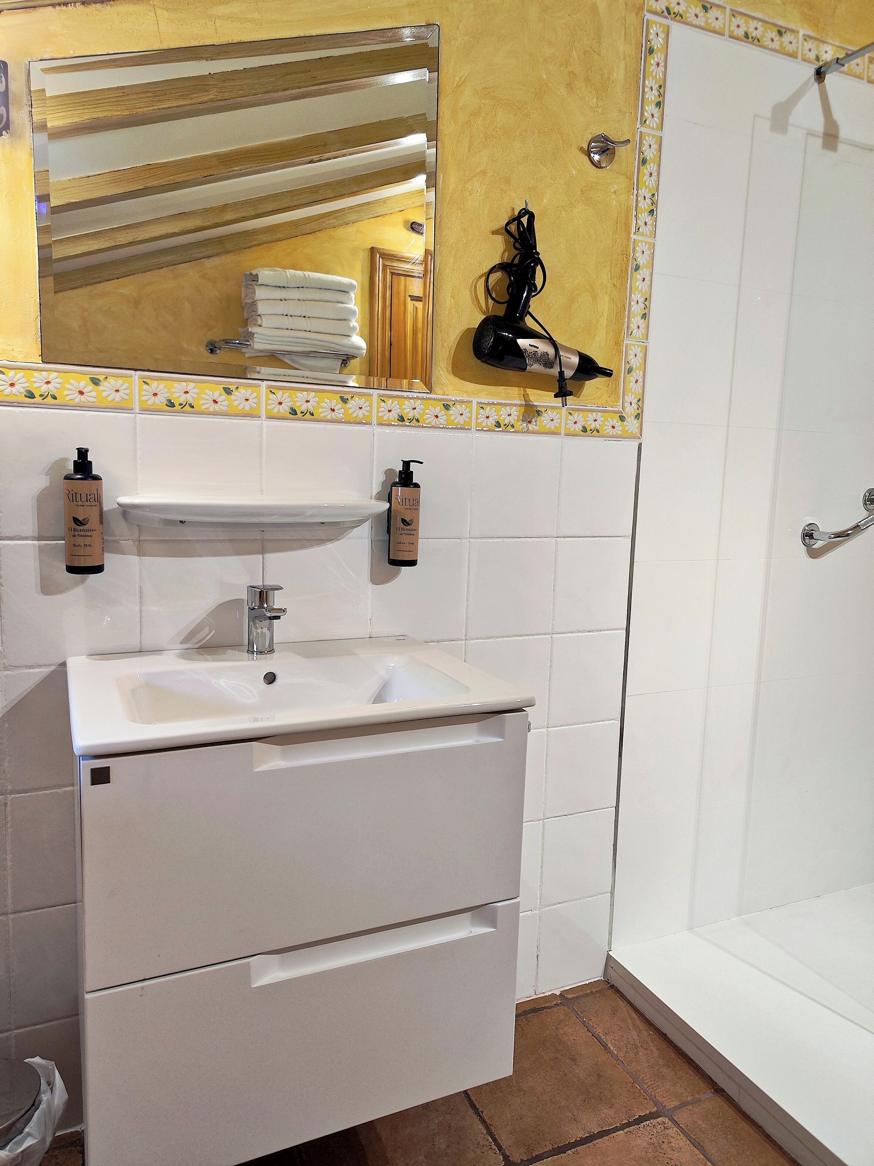 A bathroom with a white sink, a mirror, and a shower. There are two bottles of Ritual body wash on the wall.