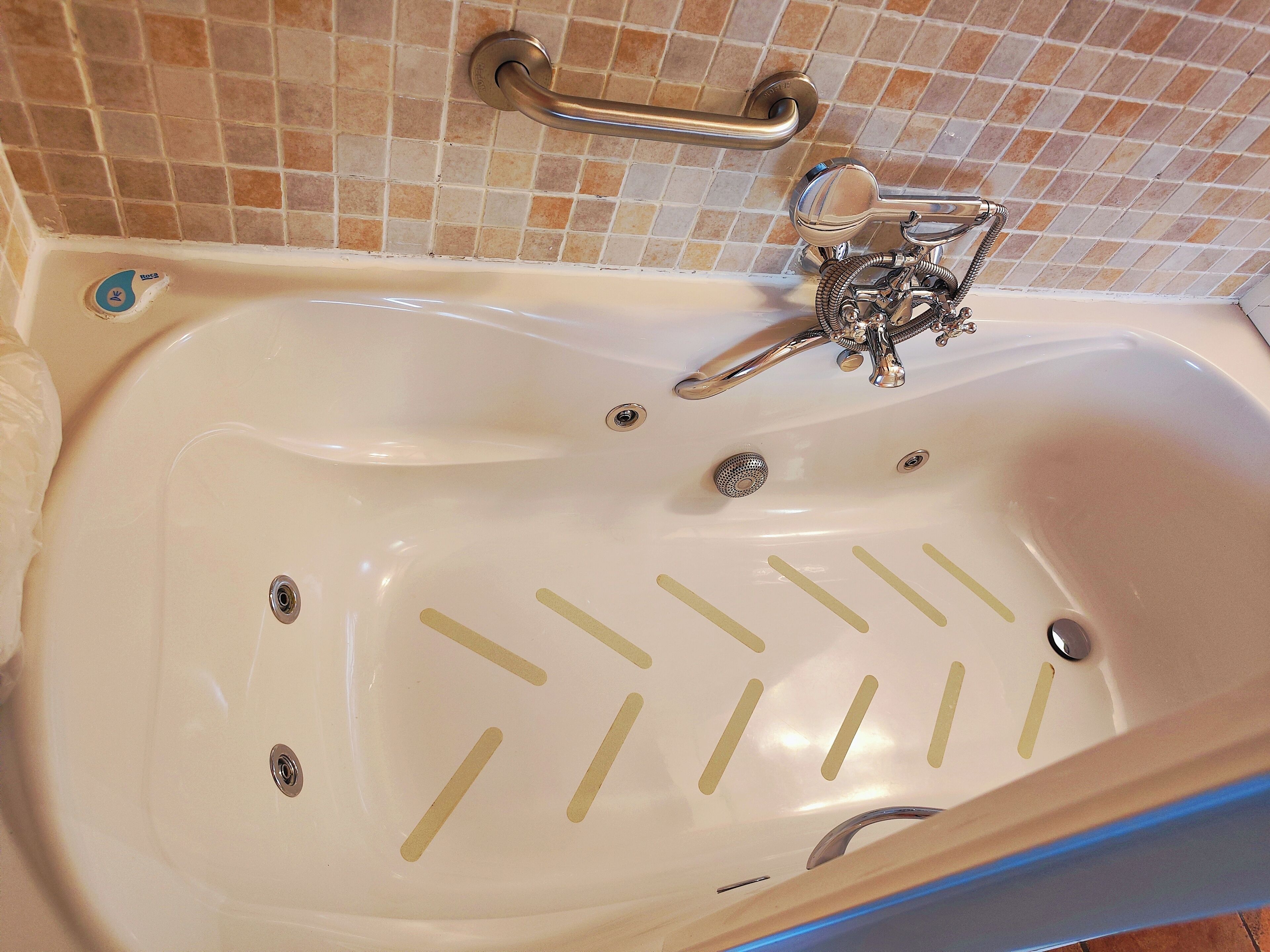 Une baignoire équipée d’un pommeau de douche à main, d’un siège intégré et d’une barre d’appui.