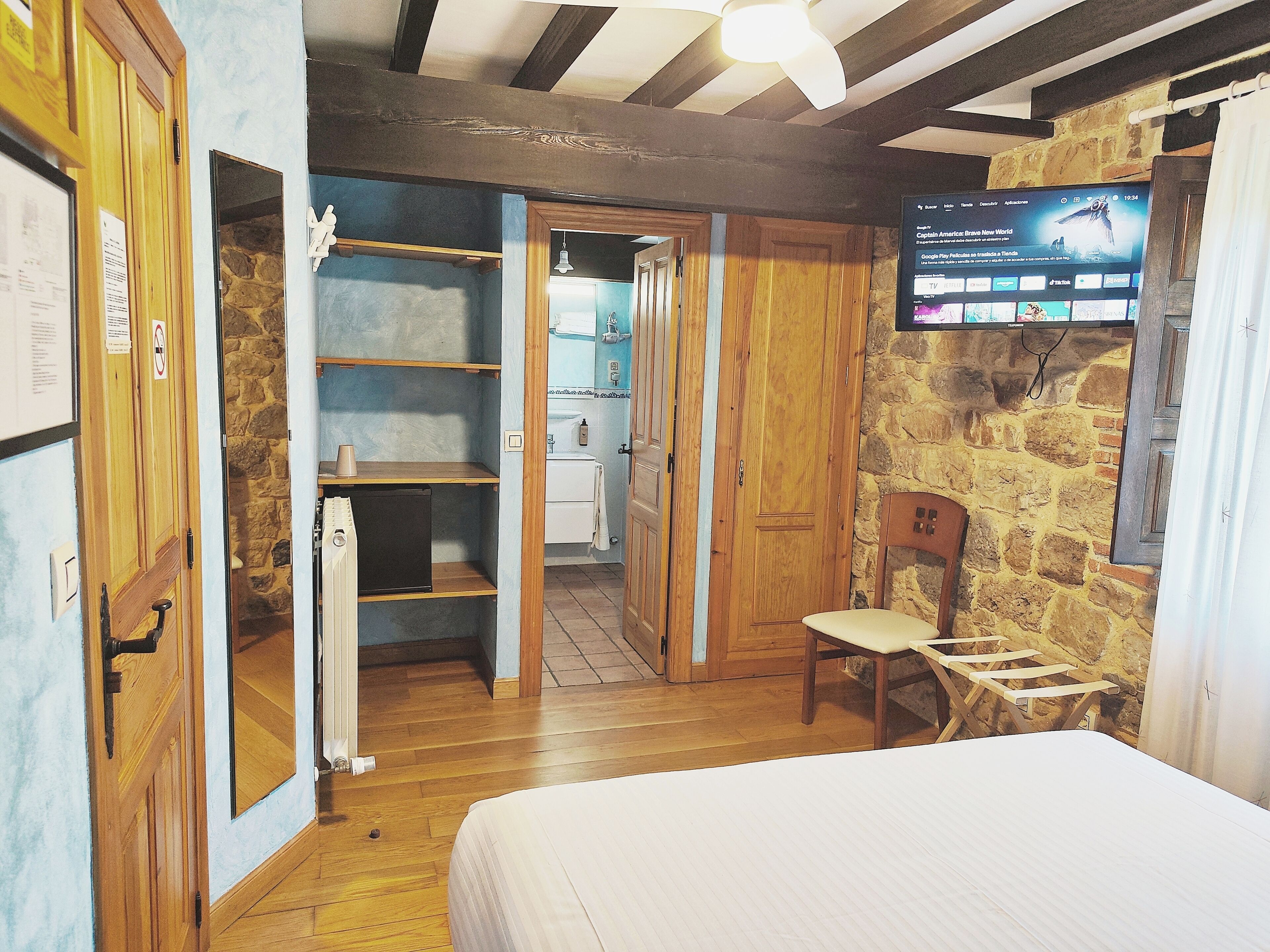 A bedroom with a bed, wooden wardrobe, and a TV mounted on the wall.