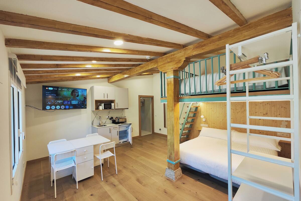 Une petite chambre comprenant un lit superposé, un coin cuisine, un bureau avec une chaise et un téléviseur fixé au mur.