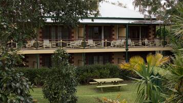 A two-story building with a balcony, surrounded by greenery and a picnic table.