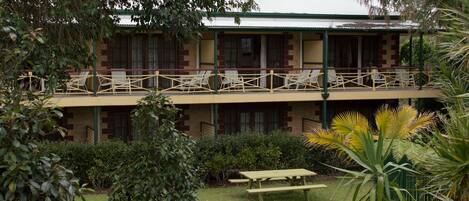 A two-story building with a balcony, surrounded by greenery and a picnic table.