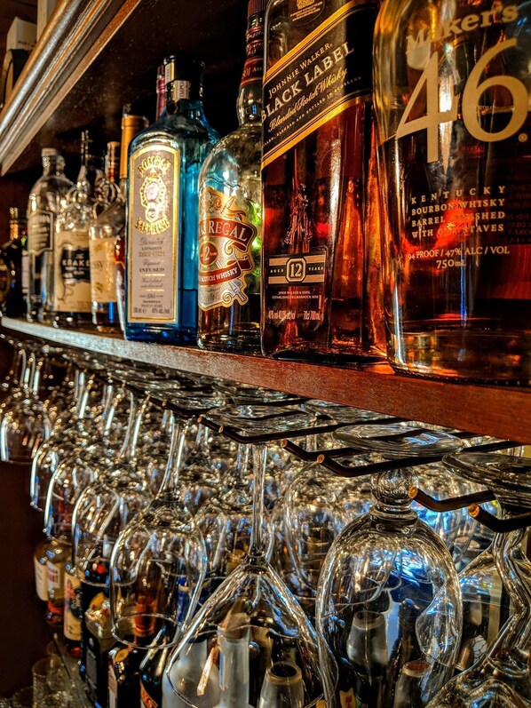 A bar with various bottles of liquor and a large number of glasses. - The Manor (Tamborine Mountain)
