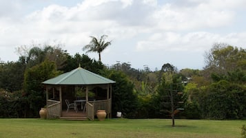 Um gazebo com telhado verde, cercado por vegetação exuberante e árvores.