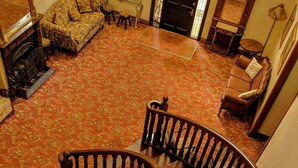 A grand staircase with ornate railings and a patterned carpet, leading to a room with a fireplace and seating area. - The Manor (Tamborine Mountain)