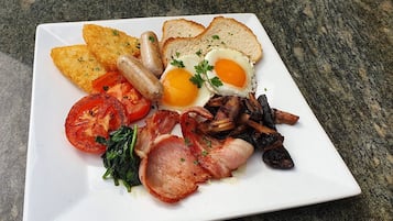 Un plato de comida para el desayuno con huevos, salchichas, tocino, tomates y tostadas.