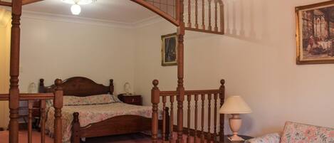 A bedroom with a wooden staircase, a bed, a nightstand, a lamp, and a floral sofa.