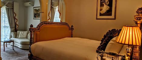 A classic hotel room with a large bed, ornate wooden headboard, a vintage telephone, and a chandelier.