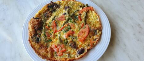 Un plat rond, de couleur brun doré, garni de légumes et d’herbes aromatiques, présenté sur une assiette blanche.