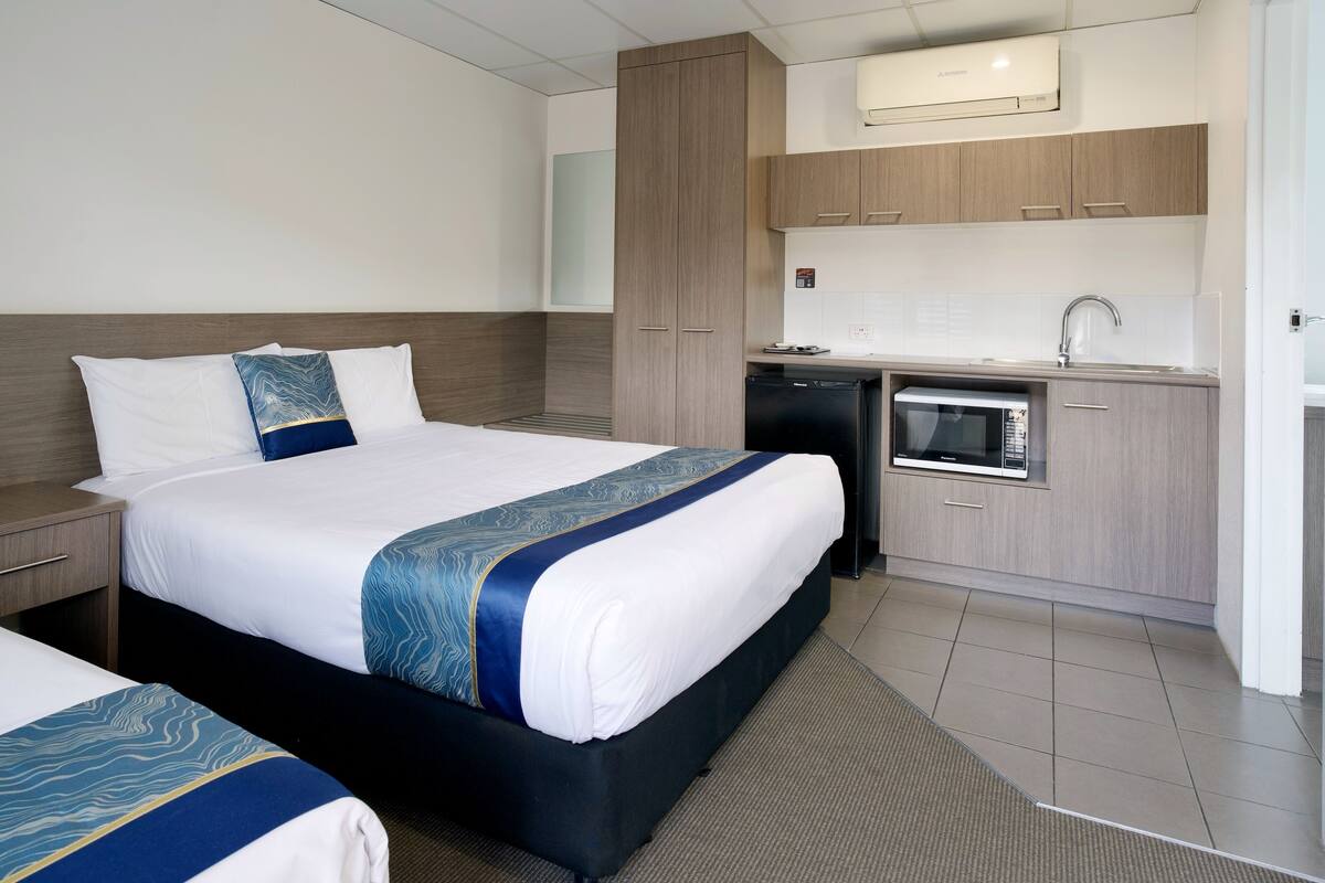 Quarto de hotel com cama, mesas de cabeceira, micro-ondas, pia e um pequeno frigorífico.