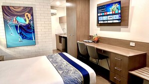 Habitación de hotel con cama, escritorio, televisor y un cuadro en la pared.
