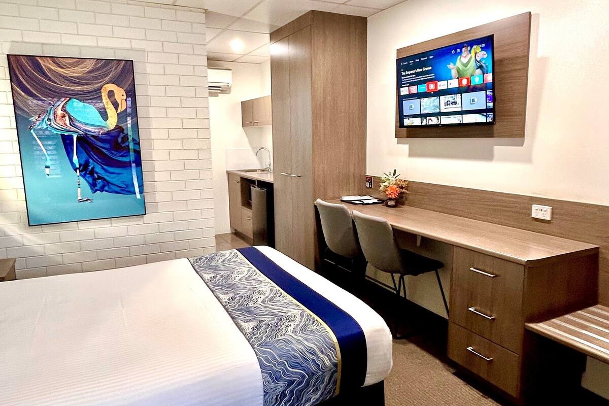 Quarto de hotel com uma cama, uma escrivaninha, uma televisão e um quadro na parede.
