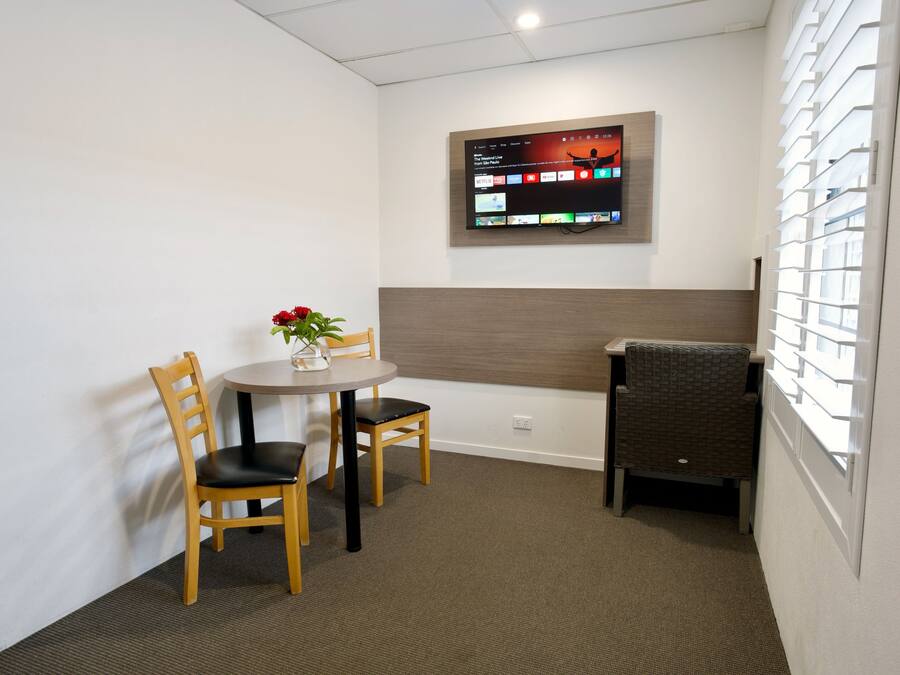 A small room with a round table, two wooden chairs, a potted plant, and a wall-mounted TV.