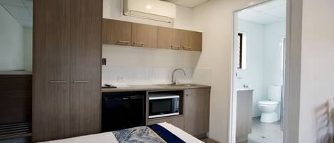 A compact hotel room with a bed, a built-in microwave, a small sink, and a separate bathroom.