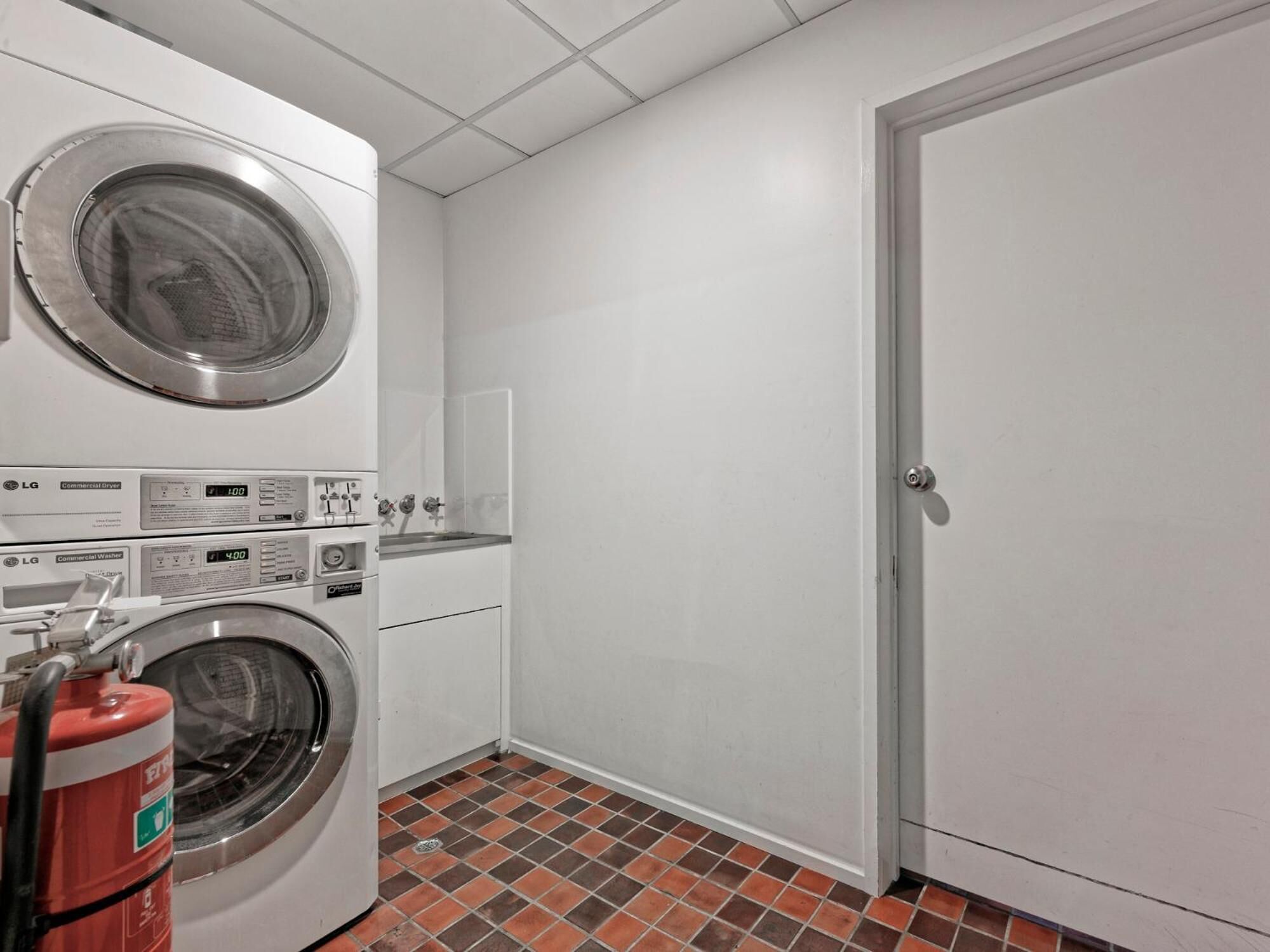 A laundry room with two LG commercial washers and dryers, a fire extinguisher, and a white door.