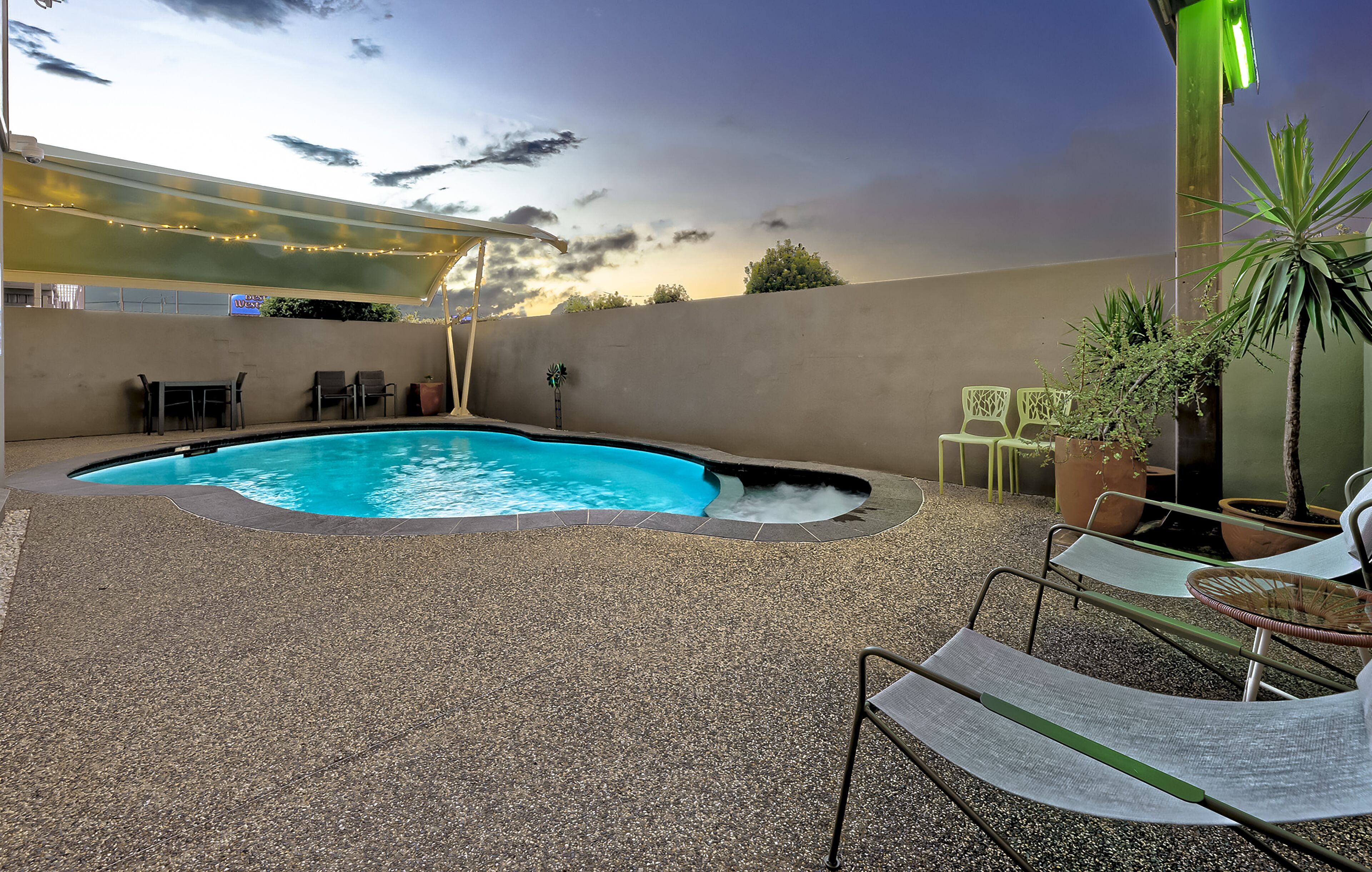 An outdoor pool area with a pebble ground, lounge chairs, and potted plants.