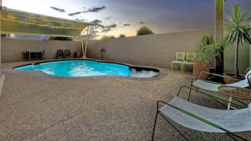 An outdoor pool area with a pebble ground, lounge chairs, and potted plants.