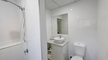 Een moderne badkamer met een glazen douchecabine, een wit wastafelmeubel en een toilet.