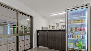Un moderno hall de hotel con un refrigerador grande repleto de bebidas, una recepción y vistas al exterior a través de un vidrio.