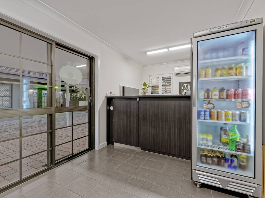 A modern hotel lobby with a large refrigerator stocked with beverages, a reception desk, and a view of the outside through a glass door.